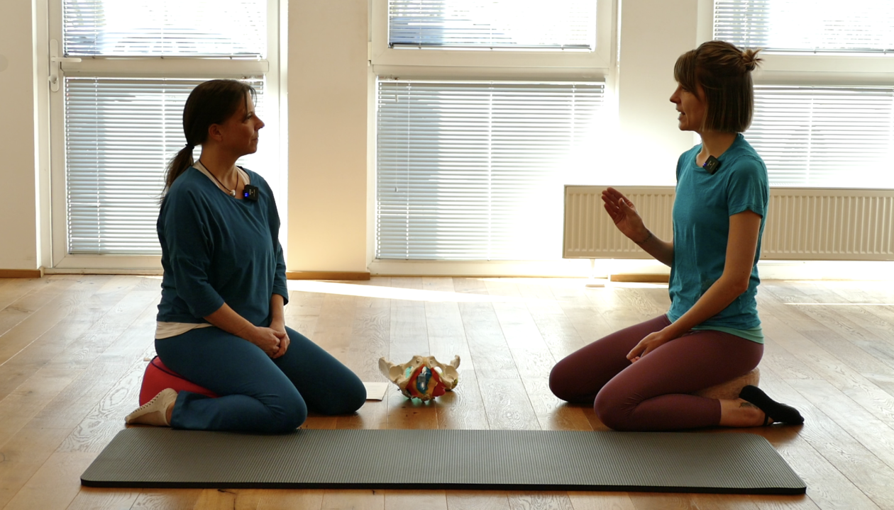 Maike Deák-Haag und Kerstin Bredehorn sitzten sich auf einem Yogakissen gegenüber, zwischen ihnen liegt ein Beckenmodell auf dem Boden