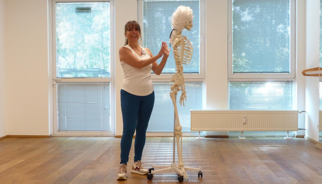 Kerstin Bredehorn steht neben einem Skelett, ihre Hände zeigen zum Rücken des Skelettes