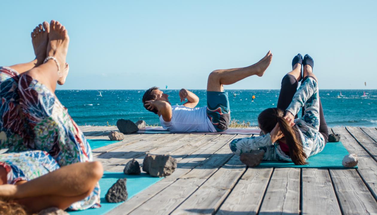 Pilates Lehrer Noun Felten mit Schülern auf einem Steg am Strand