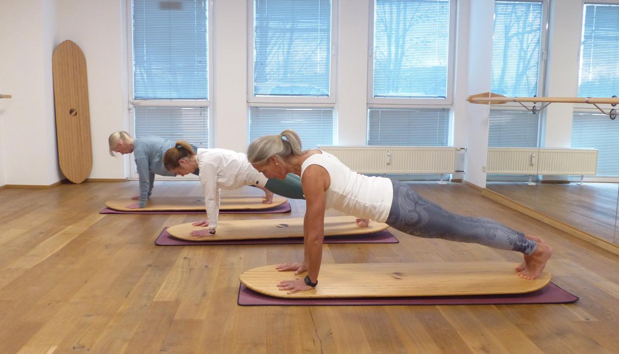 Sarah Iken und zwei Teilnehmerinnen sind in der Planke auf einem Balanceboard