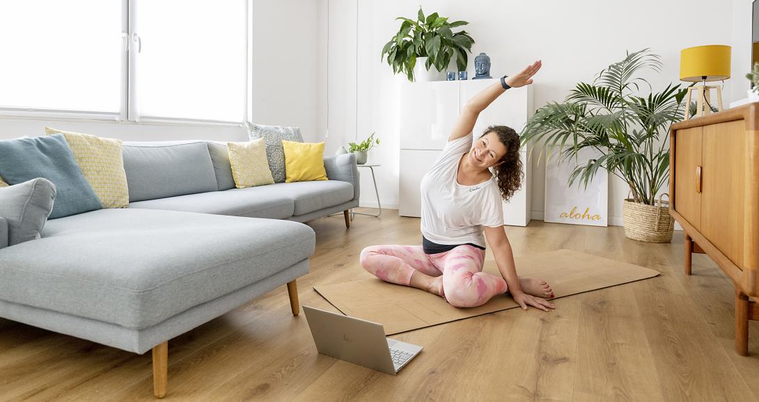 Eine Frau liegt auf einer Matte im Wohnzimmer vor einer Couch und macht Pilatesübungen